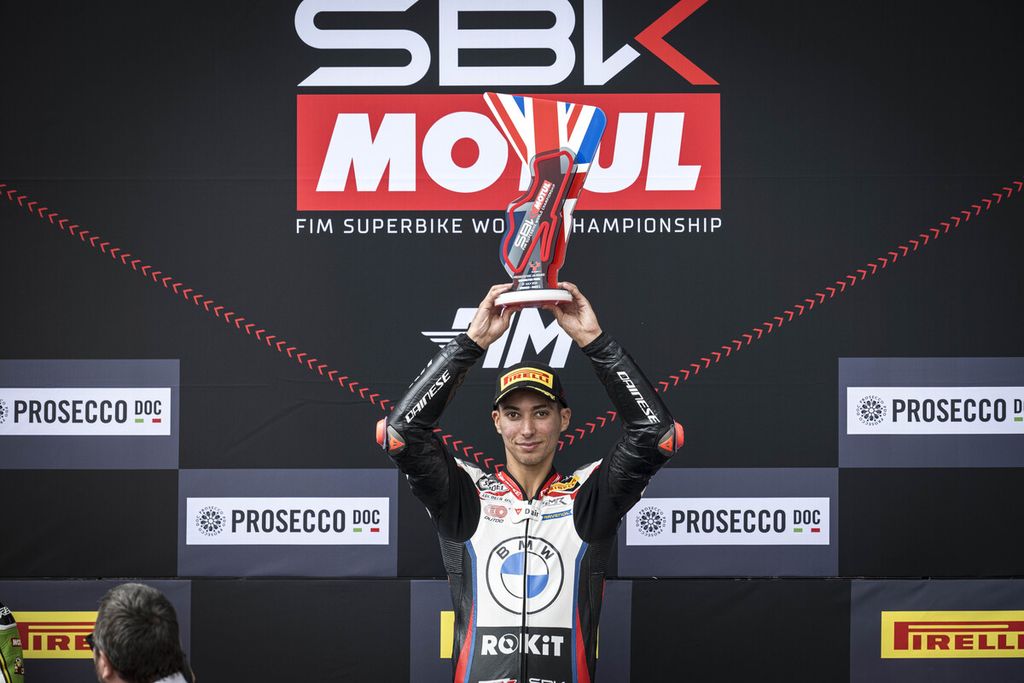 Pebalap tim Rokit BMW Motorrad WorldSBK, Toprak Razgatlioglu, mengangkat trofi seusai memenangi balapan 1 Superbike seri Inggris di Sirkuit Donington Park, Sabtu (13/7/2024). 